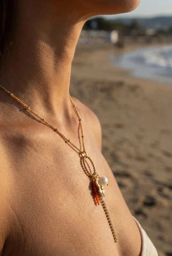 Collier doré breloque corail orange et perle nacrée porté sur plage